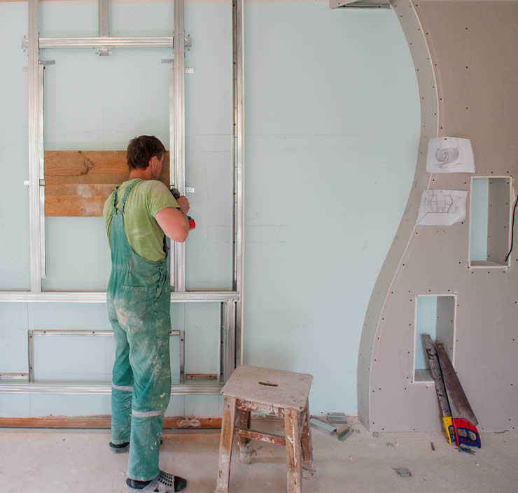 Un obrero atornilla una estructura metálica. A su lado hay una pared decorativa de pladur con una forma irregular.